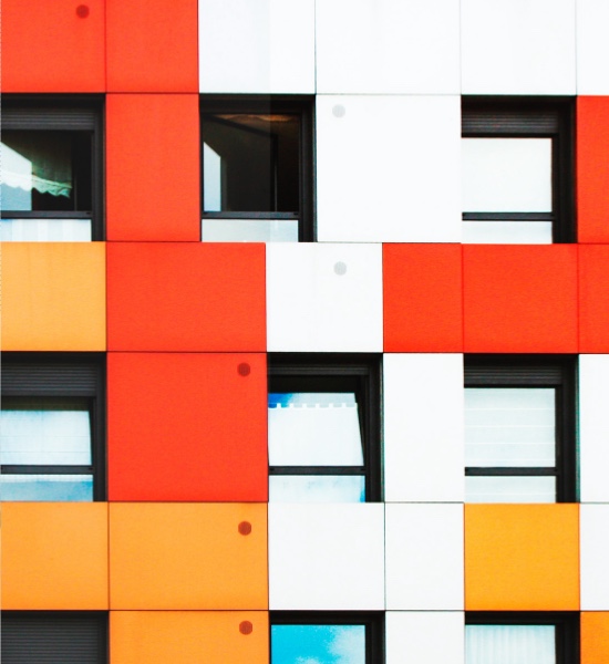 Eine Seite eines Mehrfamilienhauses mit geometrischen Formen in Rot, Orange und Weiss.