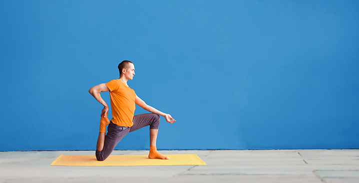 Man doing kneeling yoga pose with blue background