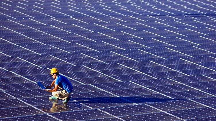 Worker holding a laptop standing on solar panels.