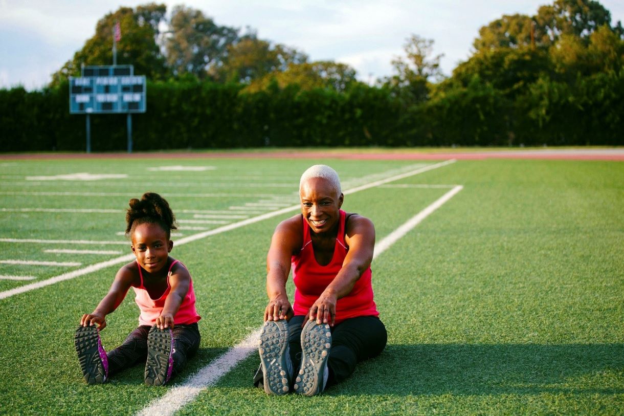 Elder woman and younger girl stretching on a football field.