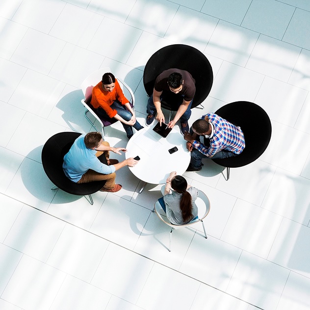 Five people seated around a table collaborating with devices
