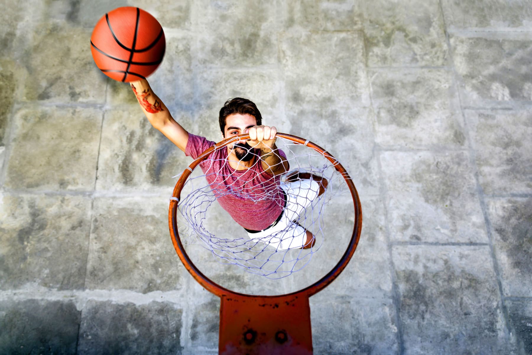 Persona lanzando un balón de baloncesto hacia el aro, vista desde arriba.