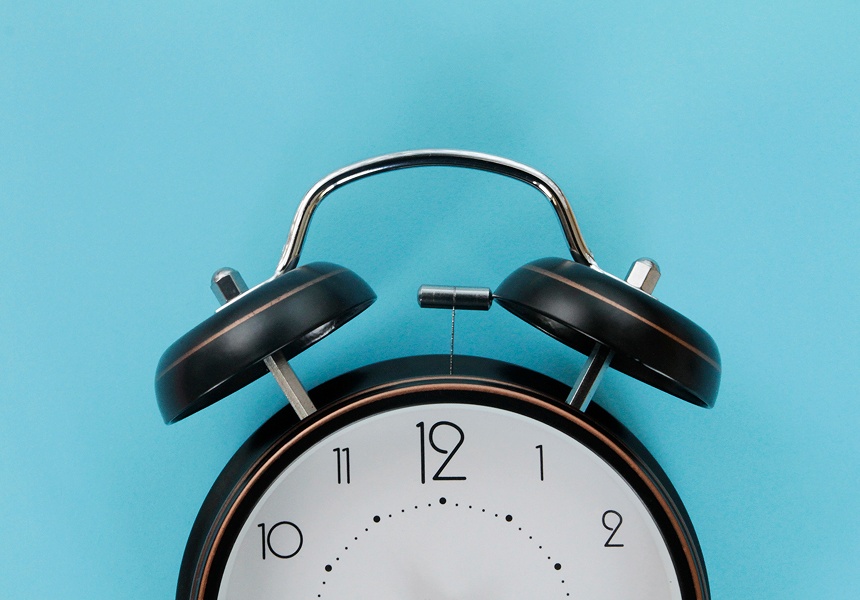 Close-up of a black analog alarm clock against a blue background.