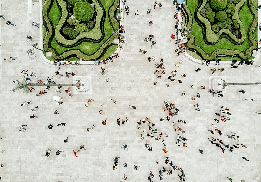 Vista aérea de personas caminando por una amplia plaza urbana rodeada de jardines verdes.