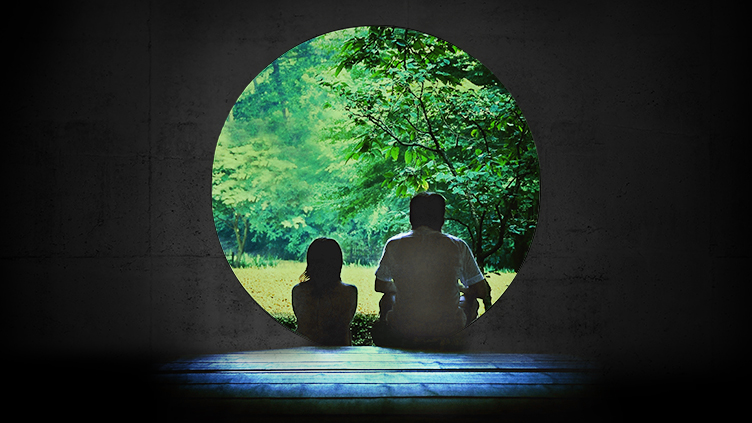 Two silhoetted people sit in front of a circular doorway, looking at green trees