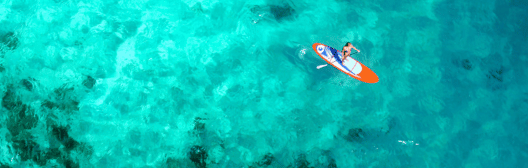 Birdeye view of a young woman on a paddleboard in open blue water.
