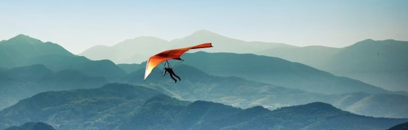 Hang glider soaring above wavy mountain ranges