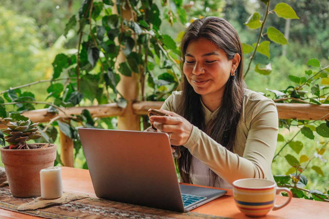 Person smiling at phone with laptop in front of them