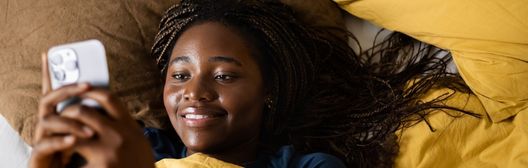 Young woman lying on a sofa and smiling while looking at her phone.