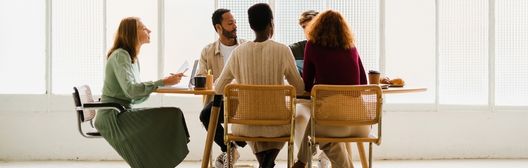 Four people seated around a table in a bright room, having a group discussion.