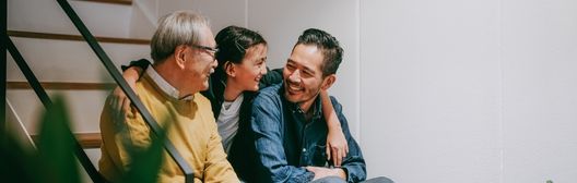 Three generations of a family sitting together on stairs, smiling and laughing.