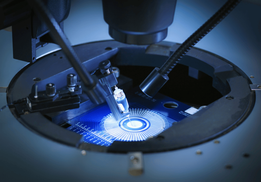 Close-up of machines inspecting a glowing microchip wafer