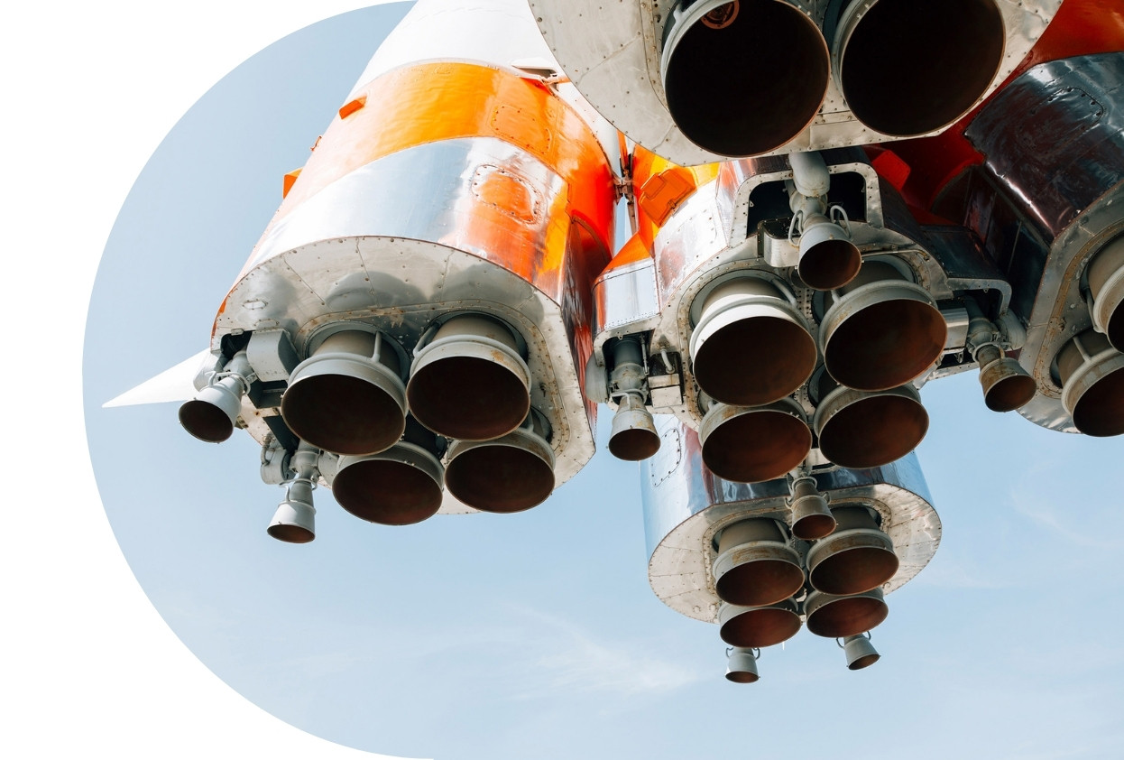 Rocket engine image. Close-up photograph of multiple rocket engines viewed from below, with orange and white rocket body panels against a pale blue sky.