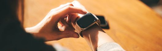 Close-up of a person tapping a smartwatch at a wooden table