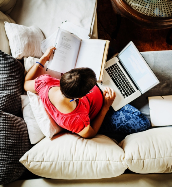 ソファでくつろぎながら、本を読み、ノートパソコンを使用している人物