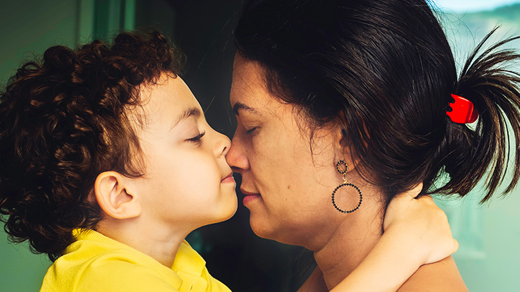A young boy in a yellow shirt touches noses with his mother.