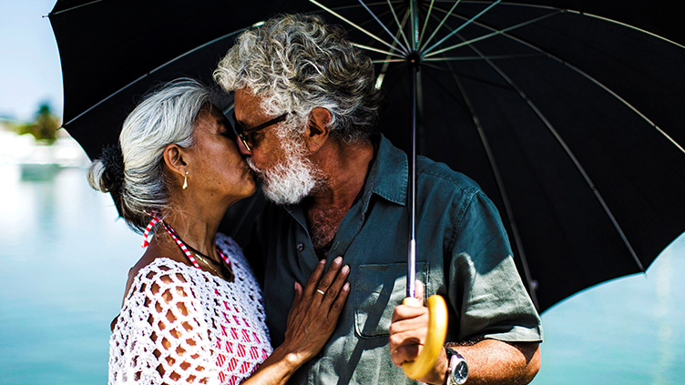 A mature couple kiss beneath a black umbrella
