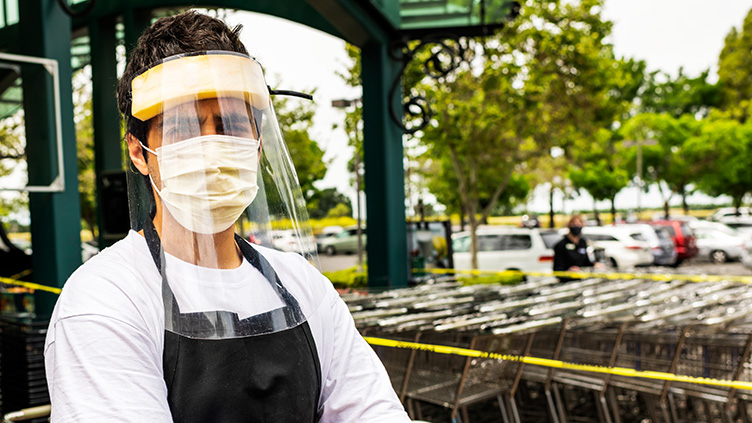A worker stands in front of shopping carts at a grocery store with a protective face mask.
