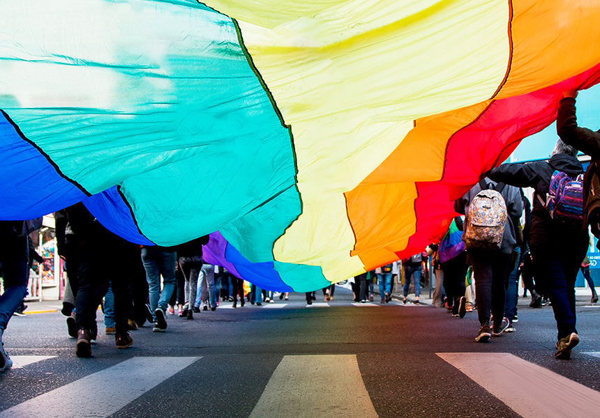 People cross a road holding a brightly colored flag.