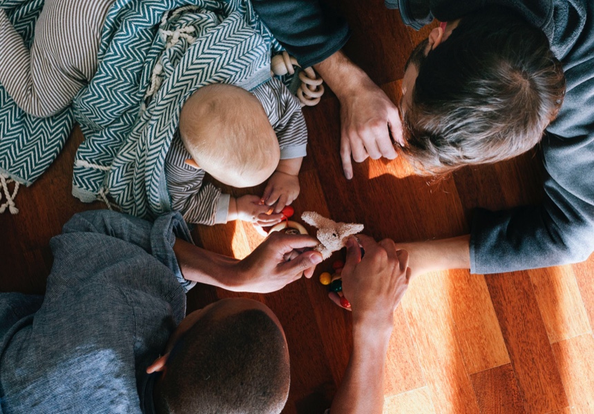 Overhead view of gay fathers playing with baby on a hardwood floor.