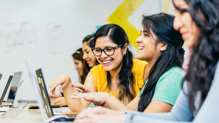 Young women work together on laptops.