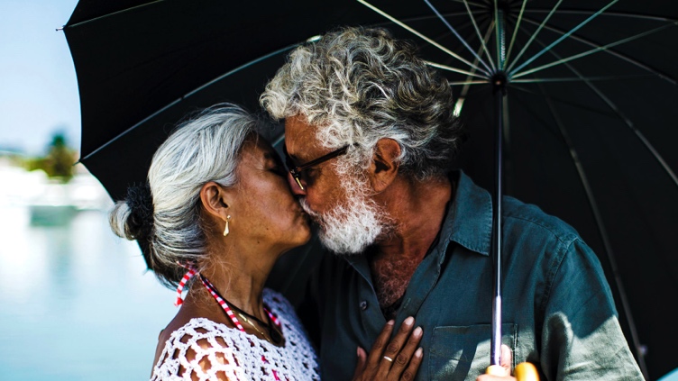 Elderly couple shares a kiss under an umbrella