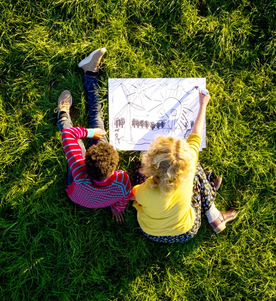 Two children sitting on the grass and drawing a picture together
