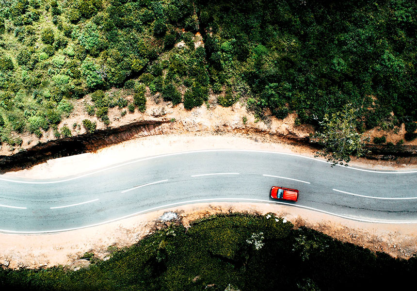 Overhead image of a car driving down a road through the mountains