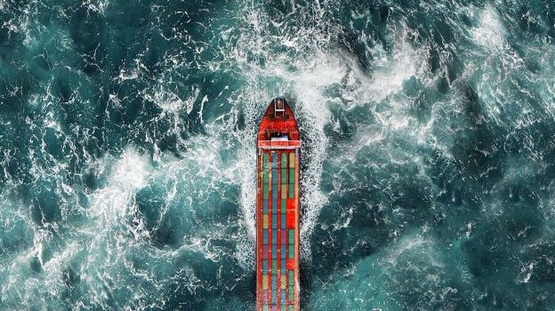 An aerial photo shows a cargo ship loaded up with colorful containers on a choppy sea.
