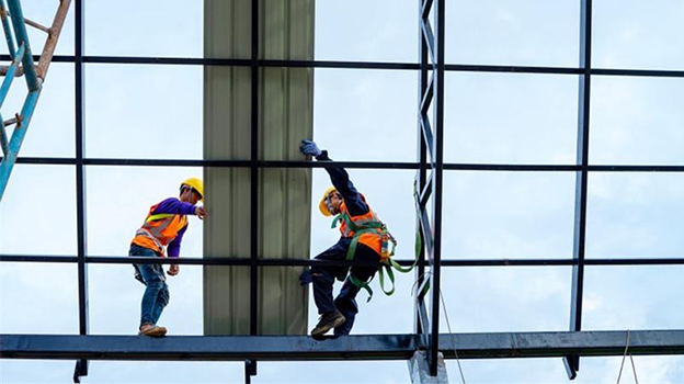 Two construction workers in safety gear installing glass panels on a high-rise building frame.