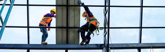 Two construction workers in safety gear installing glass panels on a high-rise building frame.