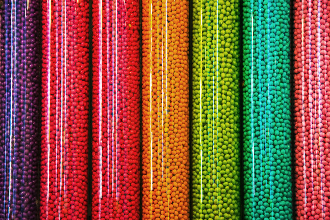 Close-up of several transparent jars arranged side by side, displaying a gradient of vibrant colors from deep purple and magenta to red, orange, yellow, and green.