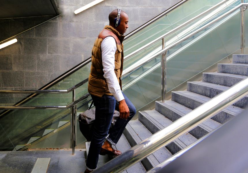 Man with headphones walking up steps with bag