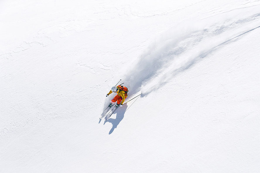Person in an orange and yellow ski suit skis across fresh snow