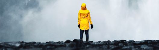 Woman in yellow raincoat in front of a waterfall.