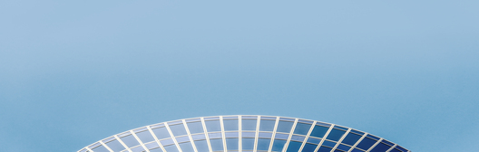 Esteban NogueyraThe top section of a curved, modern building with a glass facade.