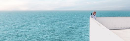 A person standing on a white wall overlooking the ocean