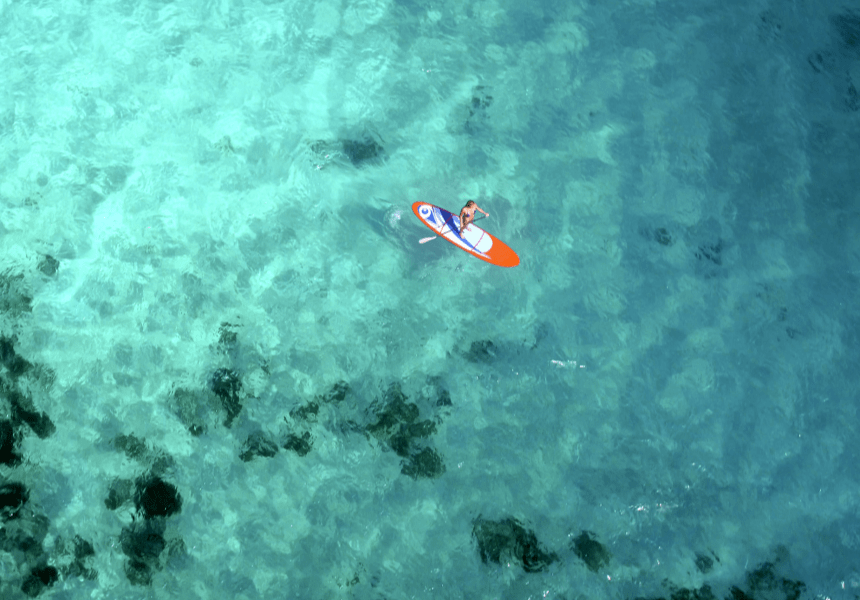 image shows a person on a paddle board in crystal clear water in the ocean.