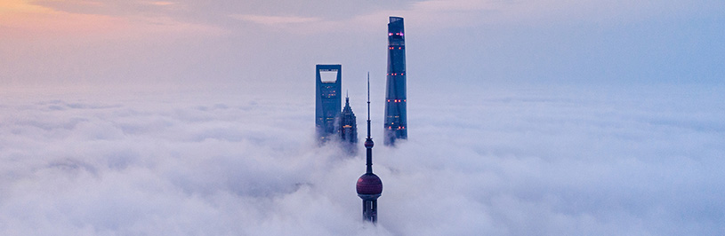 Two tall buildings rise above a cloud-covered sky, creating a striking contrast against the soft, white clouds.