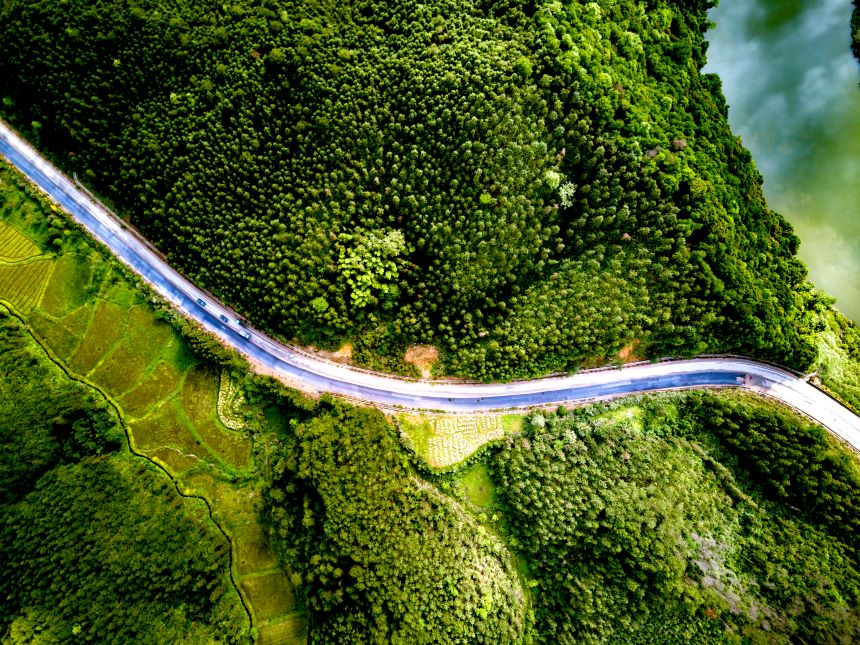 Aerial view of a double lane road cutting through a green valley surrounded by hills and trees