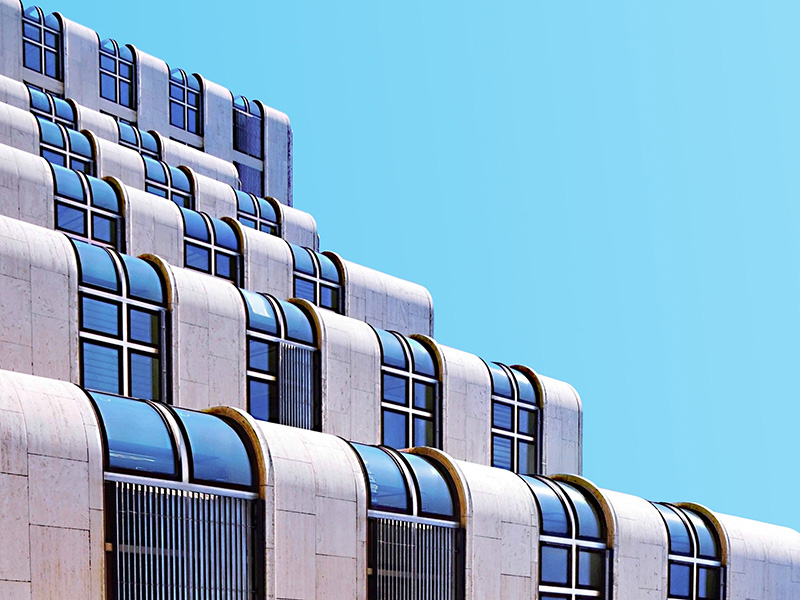 Modern building facade with repeating curved windows and blue-tinted glass panels against a bright blue sky