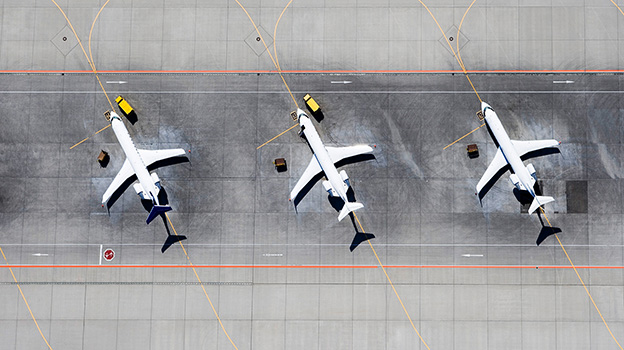 Aerial view of three parked airplanes aligned on an airport tarmac with service vehicles nearby.
