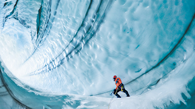 Person wearing climbing gear navigating inside a massive ice cave with curved, textured walls