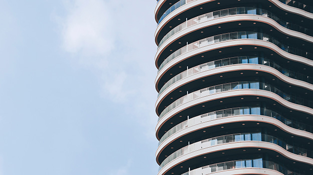 Close-up view of a modern high-rise building with curved balconies against a clear blue sky