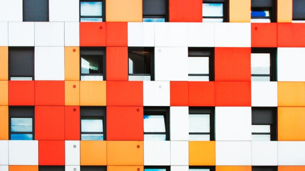 Geometric building facade with alternating orange, white, and yellow panels and rectangular windows.