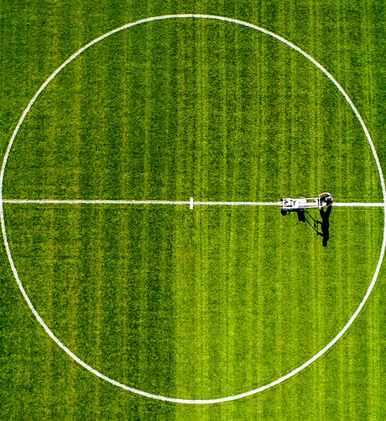 Aerial view of a green sports field with a white center circle and a groundskeeping vehicle on the grass