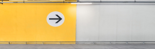 Empty indoor parking structure with a large yellow wall featuring a right‑pointing arrow.