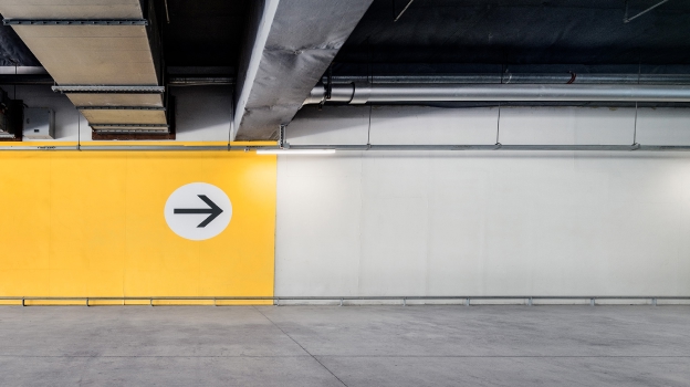 Empty indoor parking structure with a large yellow wall featuring a right‑pointing arrow.