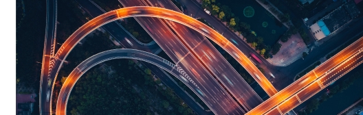 Aerial view of a multi-level highway interchange at night, with curved overpasses and flowing light trails from traffic.