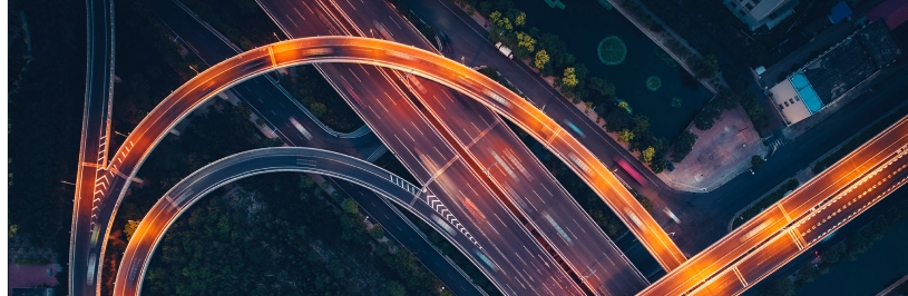 Aerial view of a multi-level highway interchange at night, with curved overpasses and flowing light trails from traffic.
